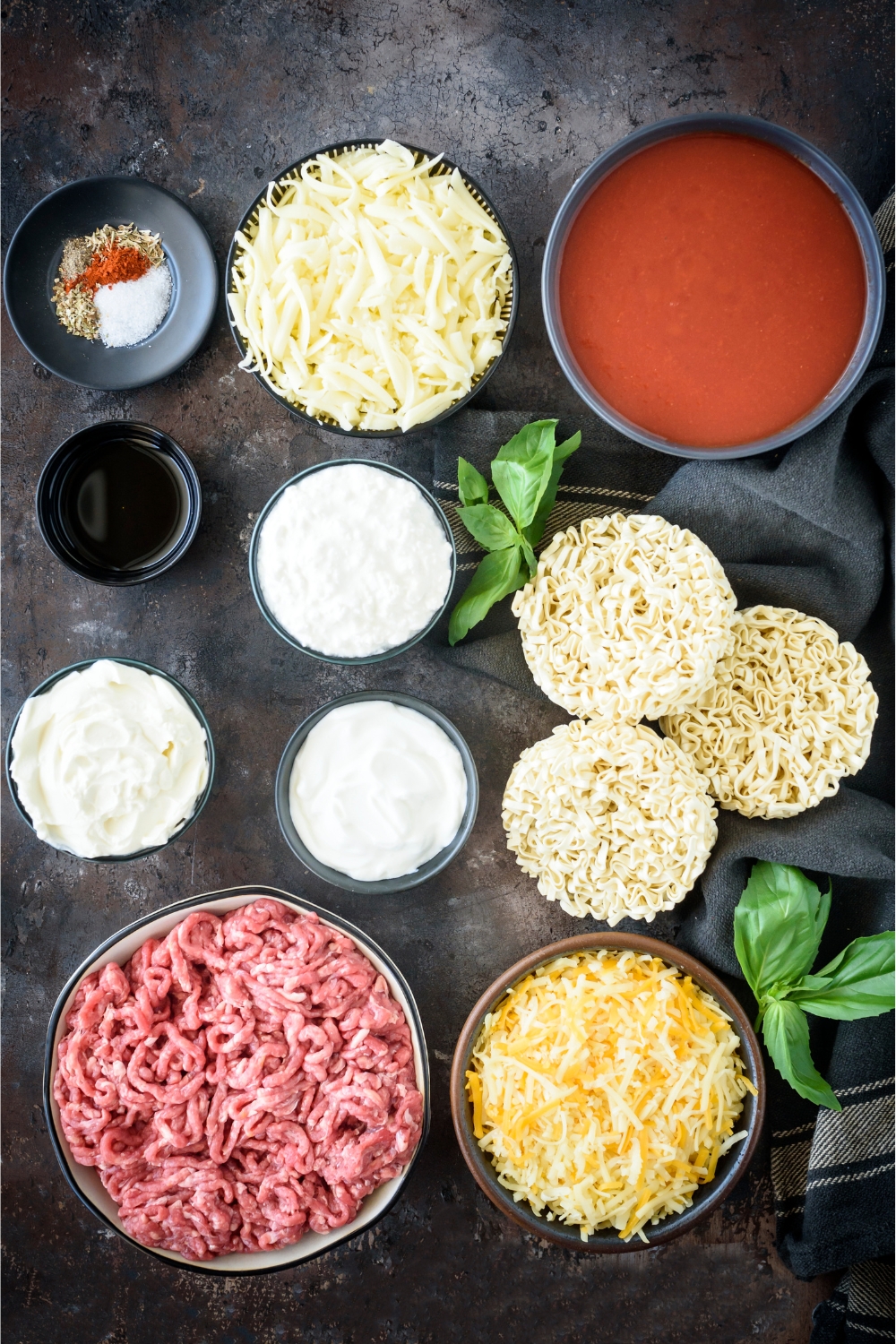 A bowl of mozzarella, a bowl of tomato soup,a bowl of cottage cheese, a bowl of yogurt, a bowl of beef, a bowl of mixed cheddar, and three bunches of egg noodles.