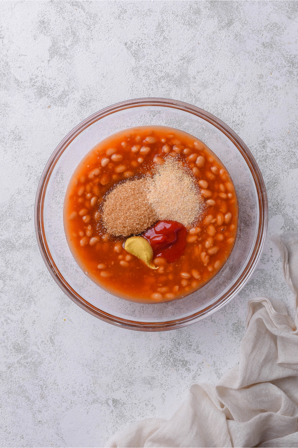 Canned beans with brown sugar, ketchup, mustard, garlic powder, and onion powder in a glass bowl.