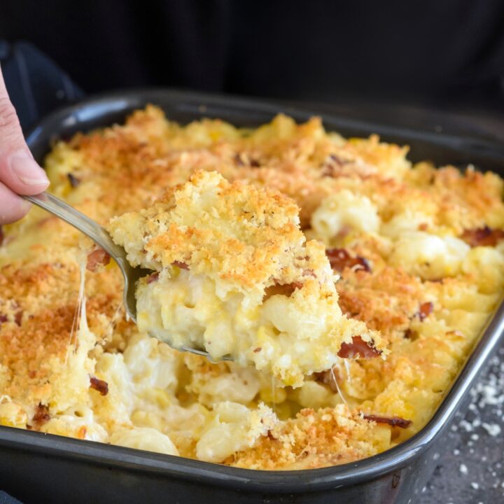 A casserole dish with macaroni corn casserole. A spoon is scooping a heaping scoop of the casserole.