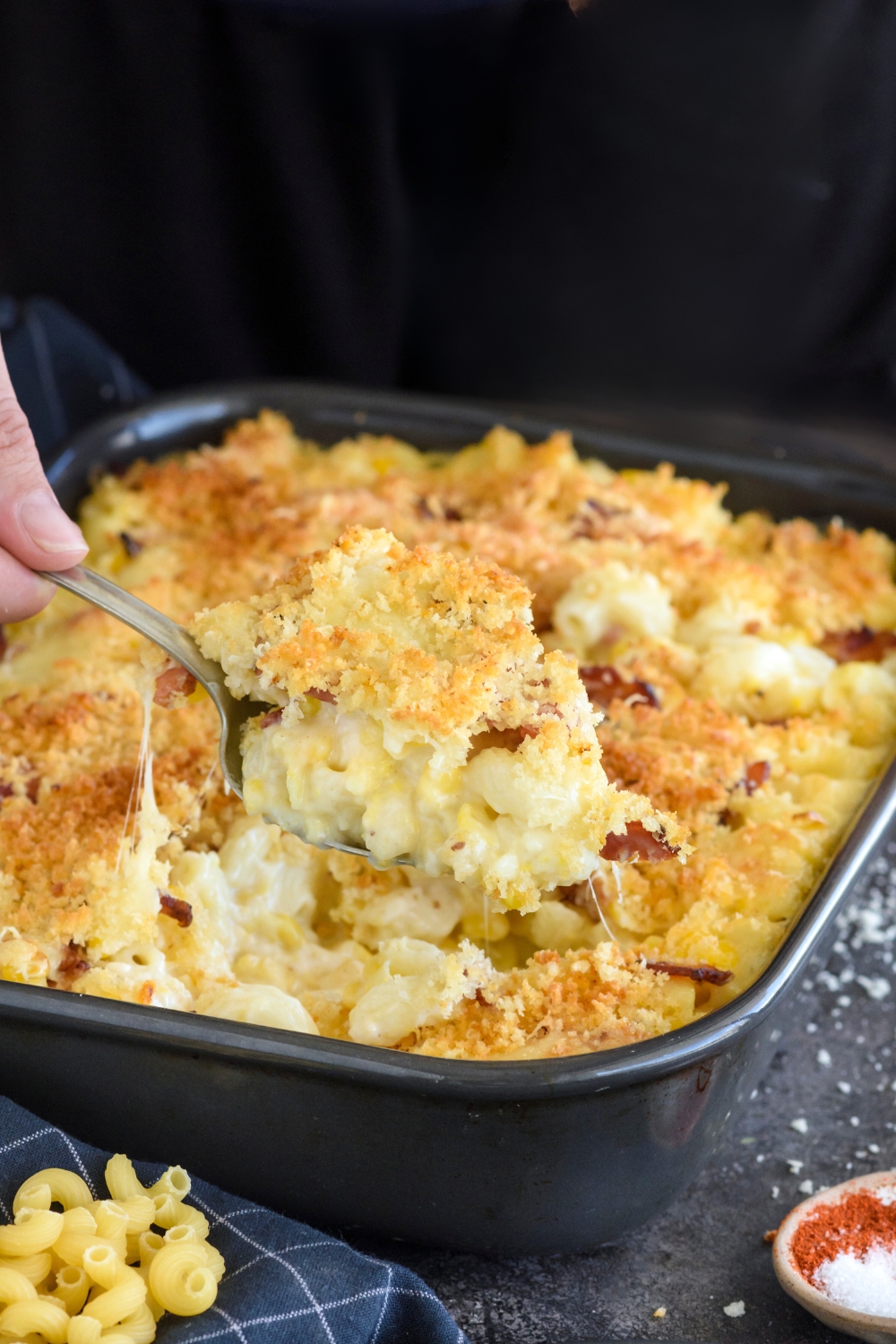 A casserole dish with macaroni corn casserole. A spoon is scooping a heaping scoop of the casserole.