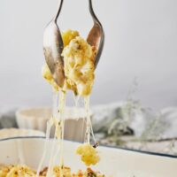 A casserole dish with two spoons scooping a serving of cheesy cauliflower.