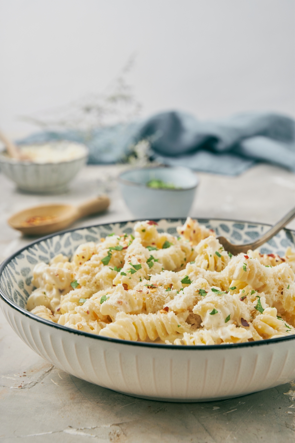A bowl of cream cheese pasta garnished with herbs, grated parmesan, and chili flakes with a fork.