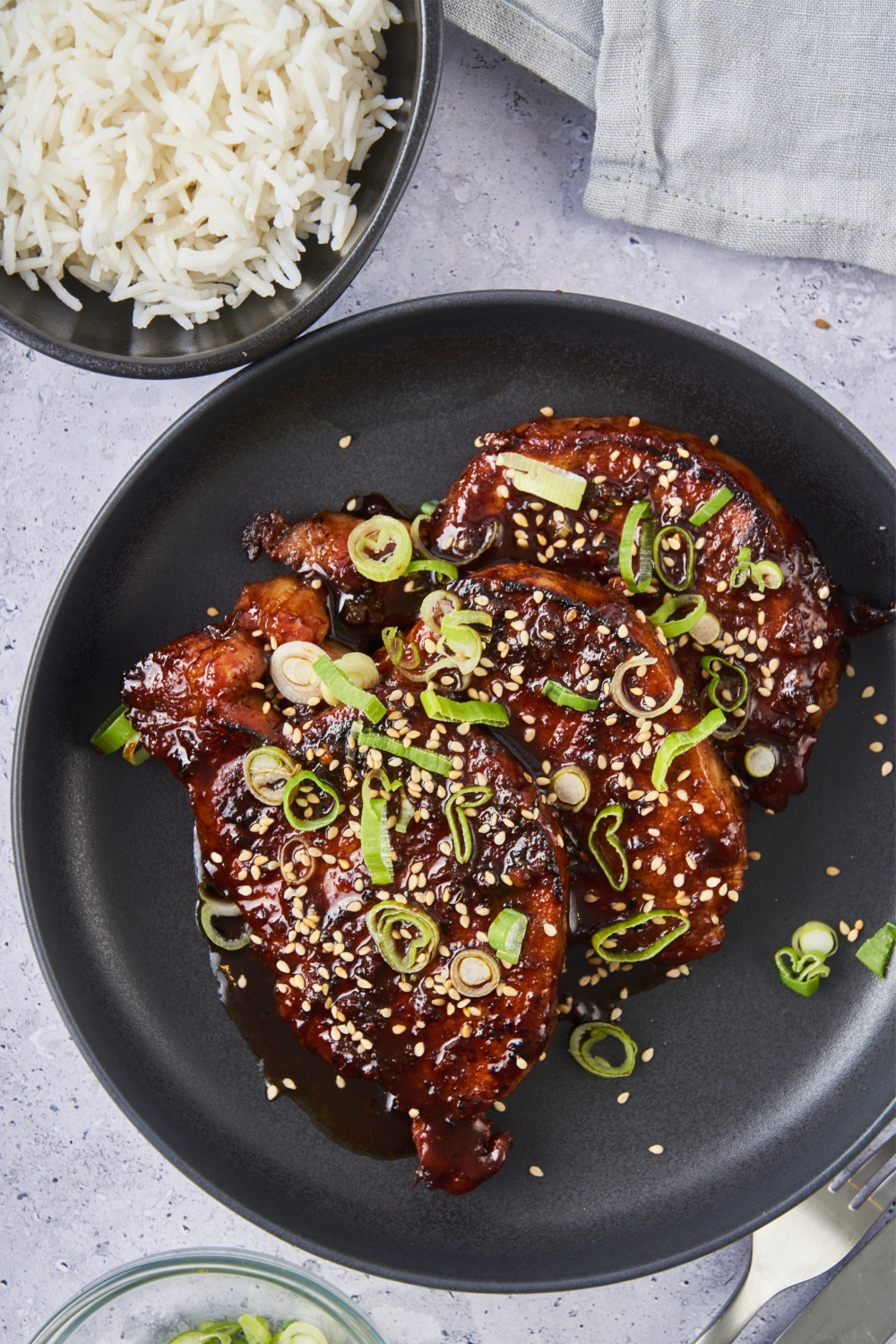 Top view of a plate of Korean pork chops garnished with chopped green onions and sesame seeds and served with a side of white rice.