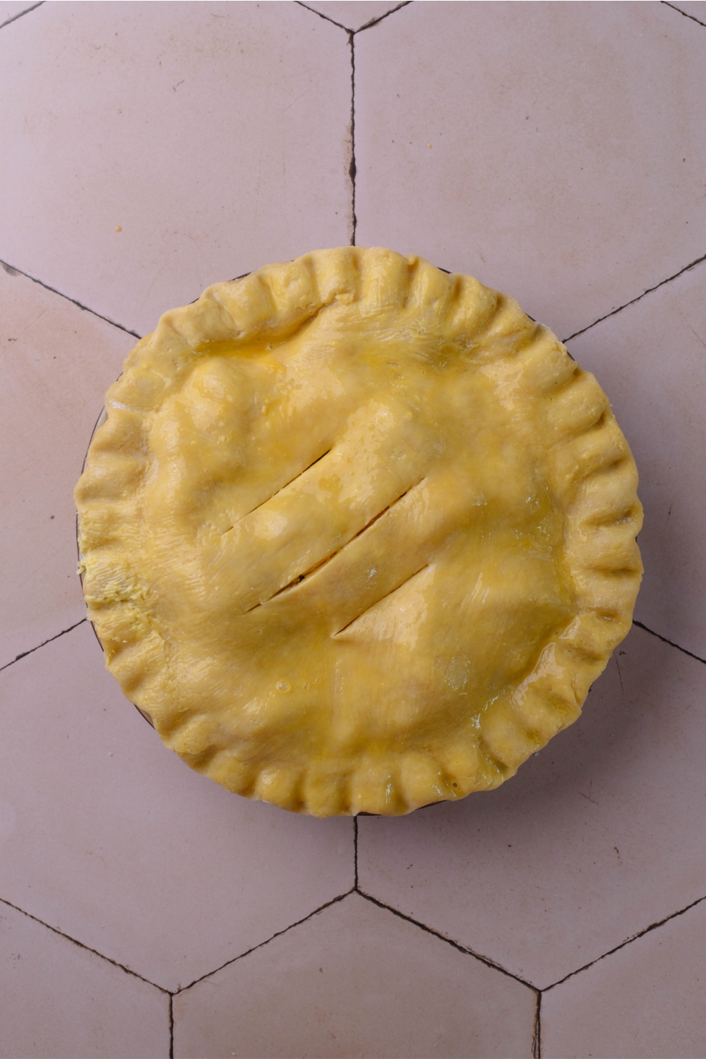 A pie pan with the top pie crust with three slits in it.