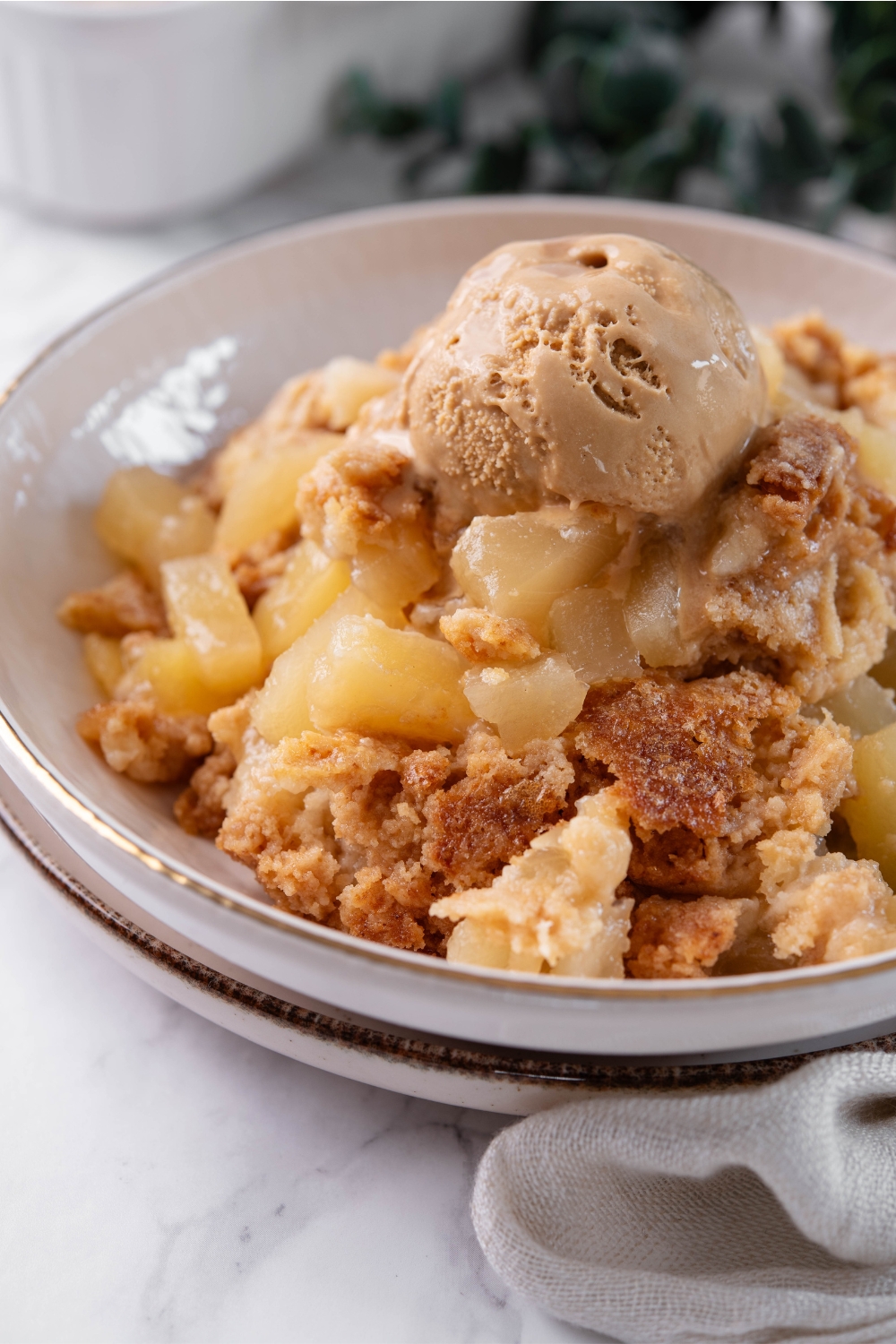 A bowl with pineapple dump cake topped with a scoop of ice cream.
