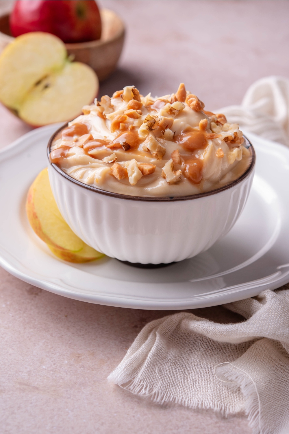 Cream cheese caramel apple dip in a white bowl that's on top of a white plate.