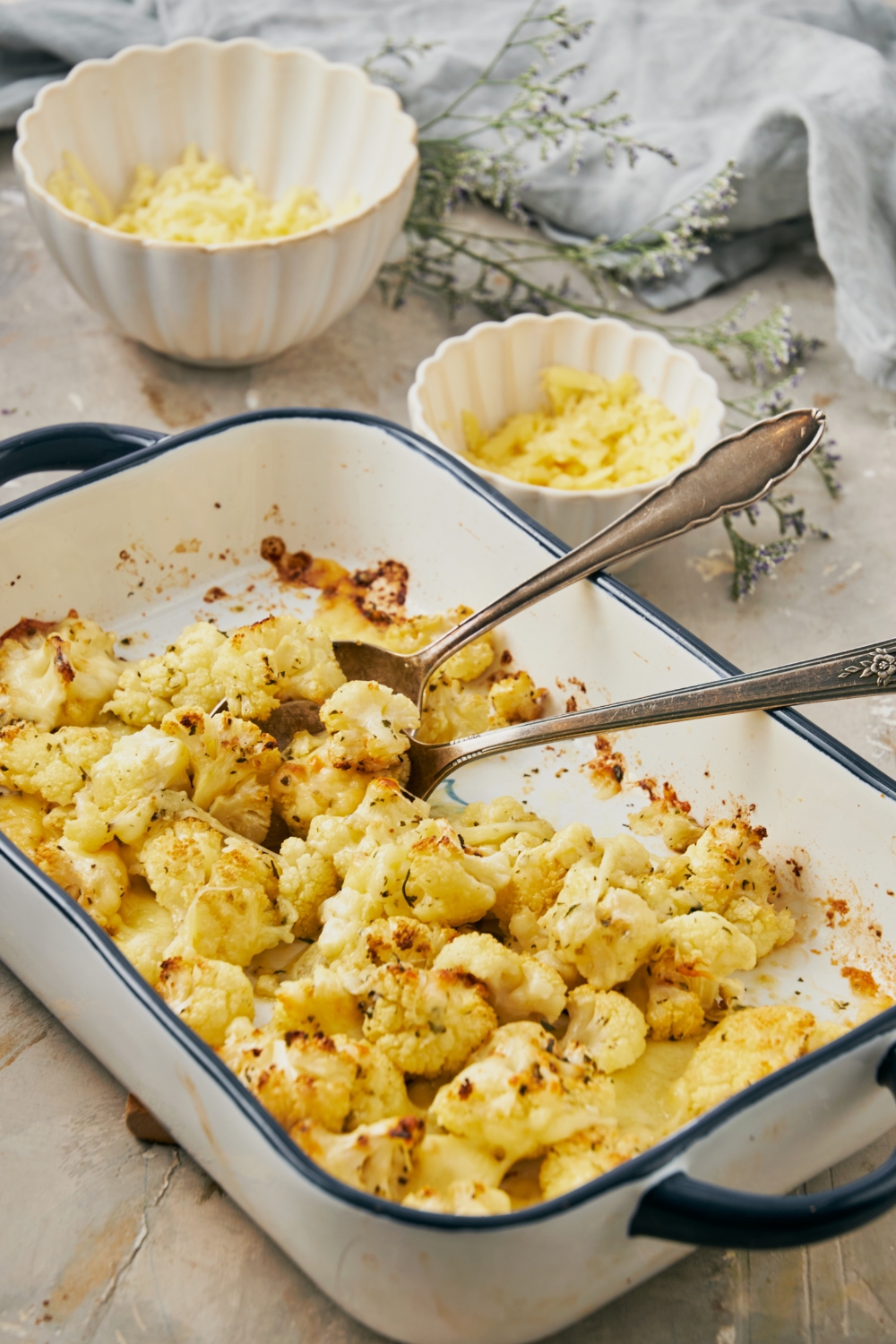 A baking dish with baked cheesy cauliflower and two spoons in it ready to serve.