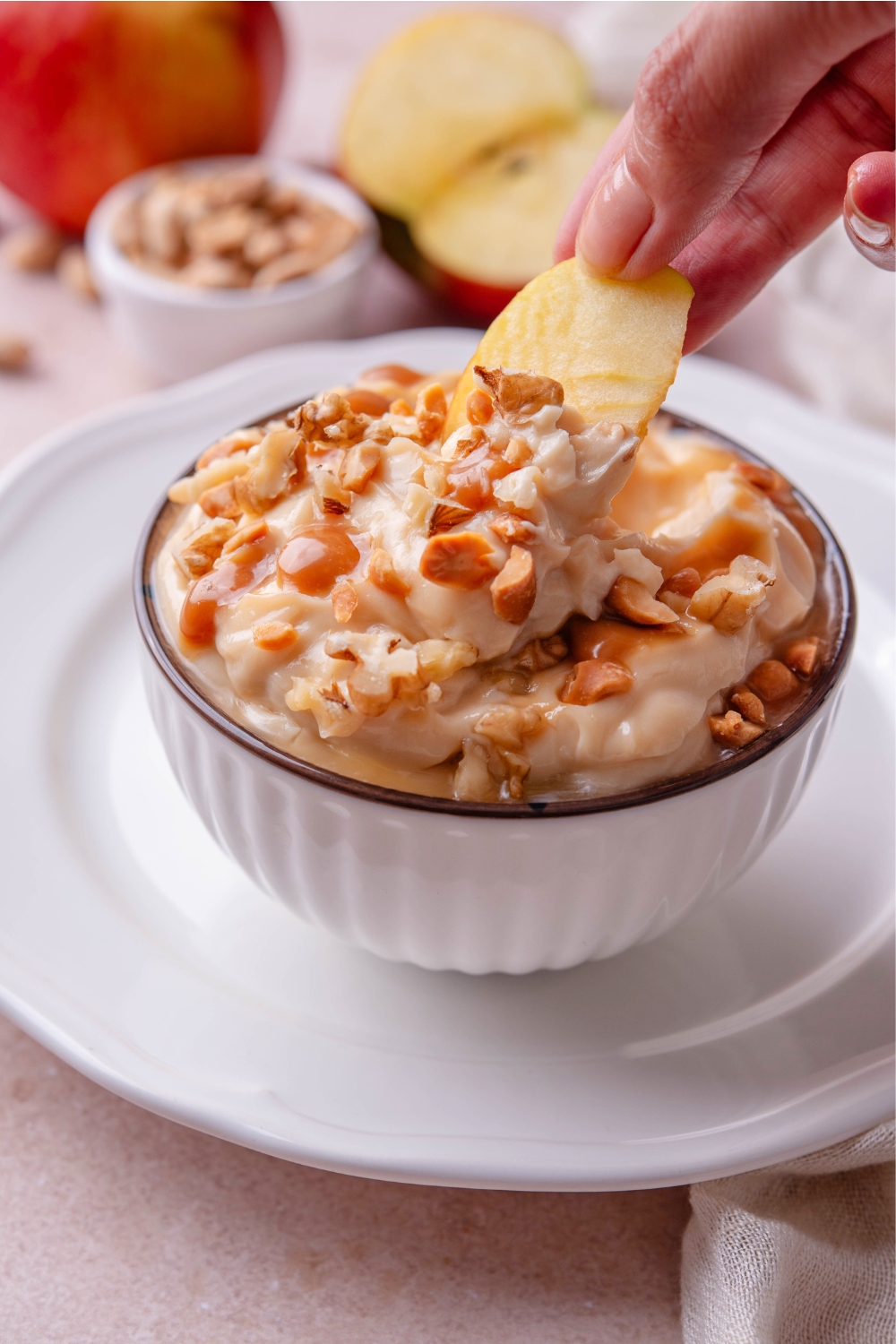 A hand dipping an apple slice into a caramel apple dip.