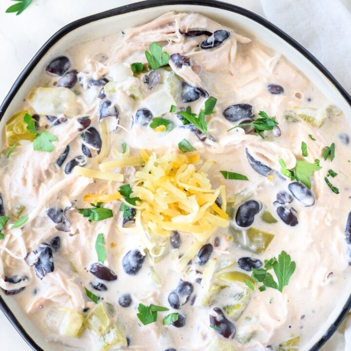 Shredded cheese on top of a cream cheese white chicken chili in a bowl on top of a white counter.