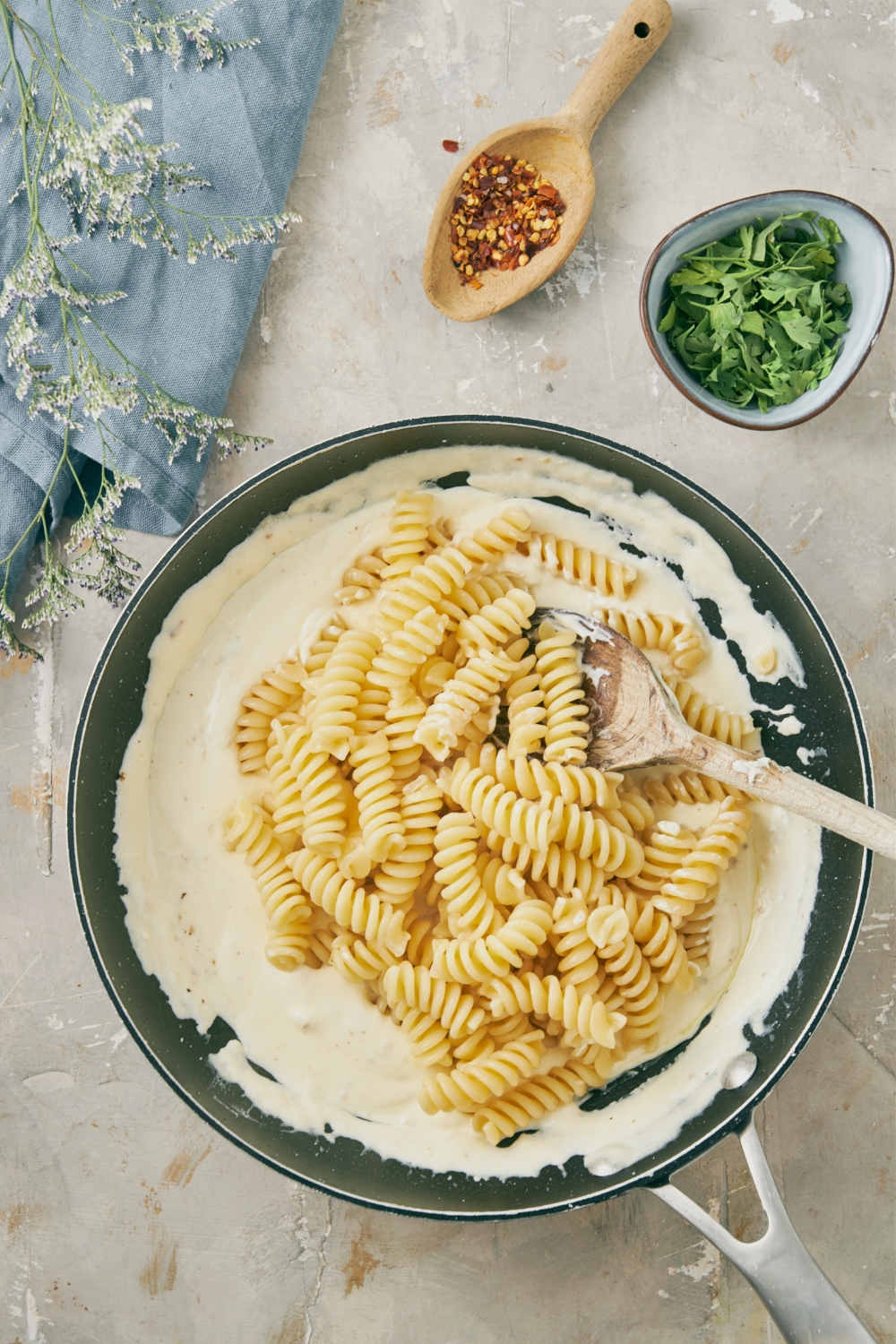 Fussili pasta being mixed with a wooden spoon in a pan filled with cream cheese sauce.