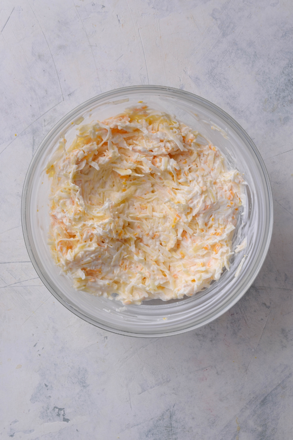 A mixing bowl with sour cream, shredded cheese, hash browns, and onion powder mixed together.