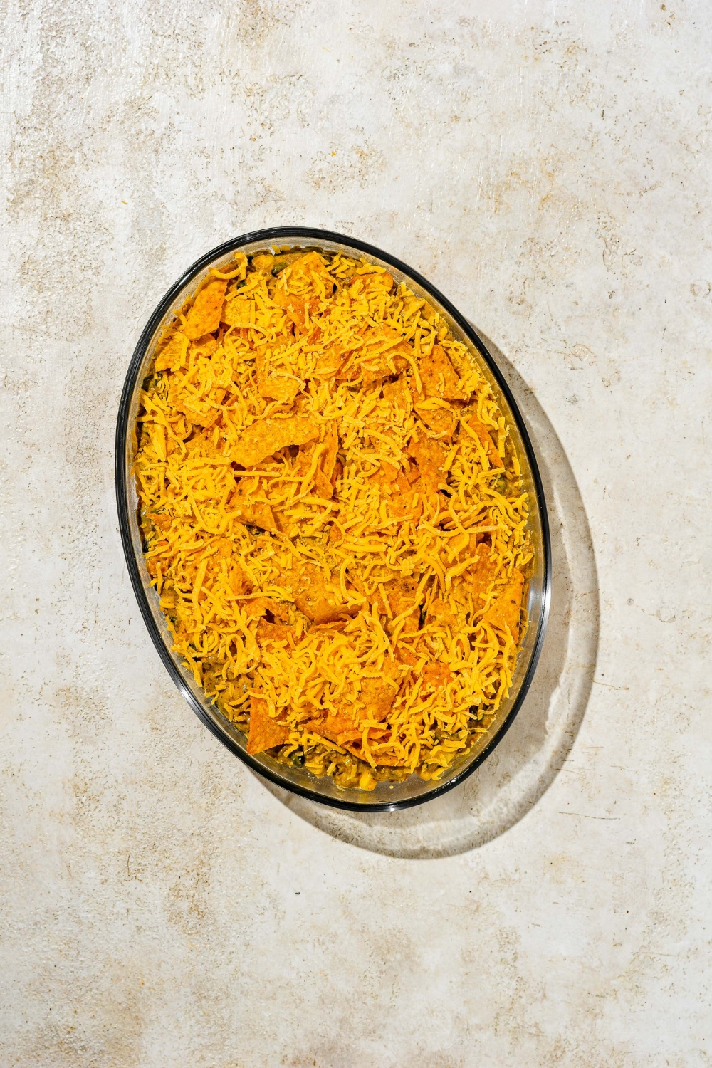 Crushed nacho cheese doritos on top of taco casserole filling in a baking dish.