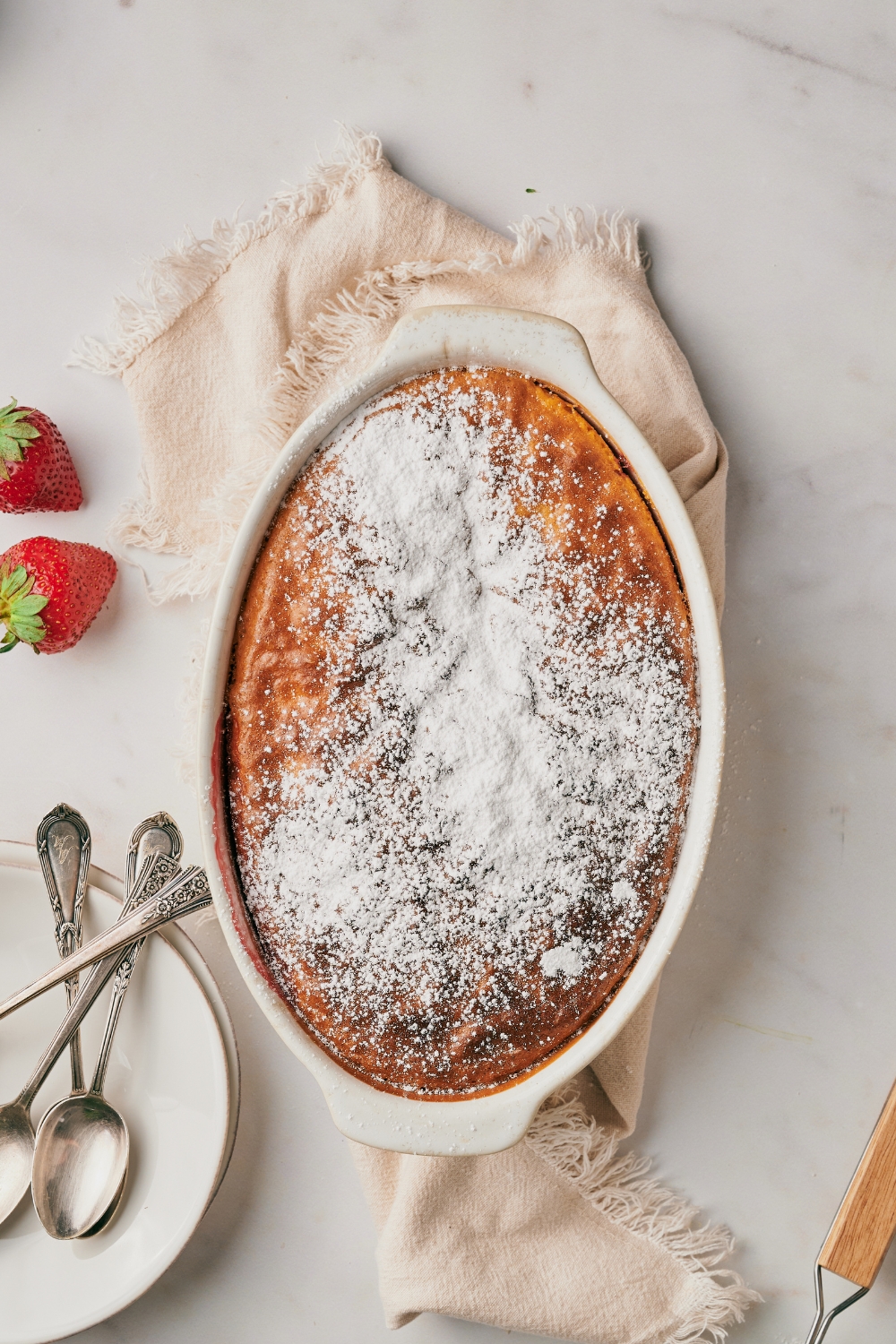 A baking dish with baked strawberry dump cake topped with powdered sugar.