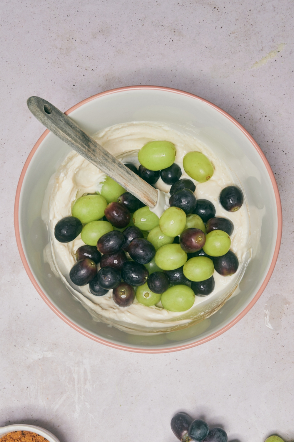 A mixing bowl with grapes being added to the cream cheese mixture.