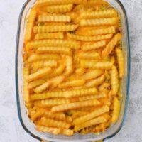 A bunch of crinkle cut french fries on top of melted cheese in a glass casserole dish on a grey counter.