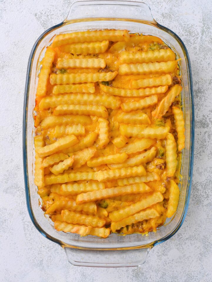 A bunch of crinkle cut french fries on top of melted cheese in a glass casserole dish on a grey counter.