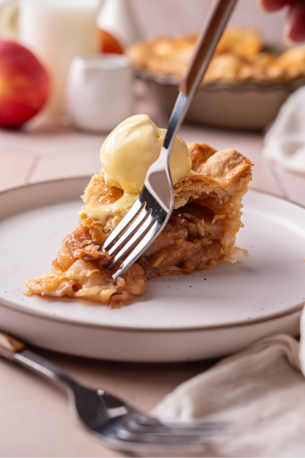 A plate with a slice of apple pie topped with a scoop of vanilla ice cream. A fork is scooping a bite.