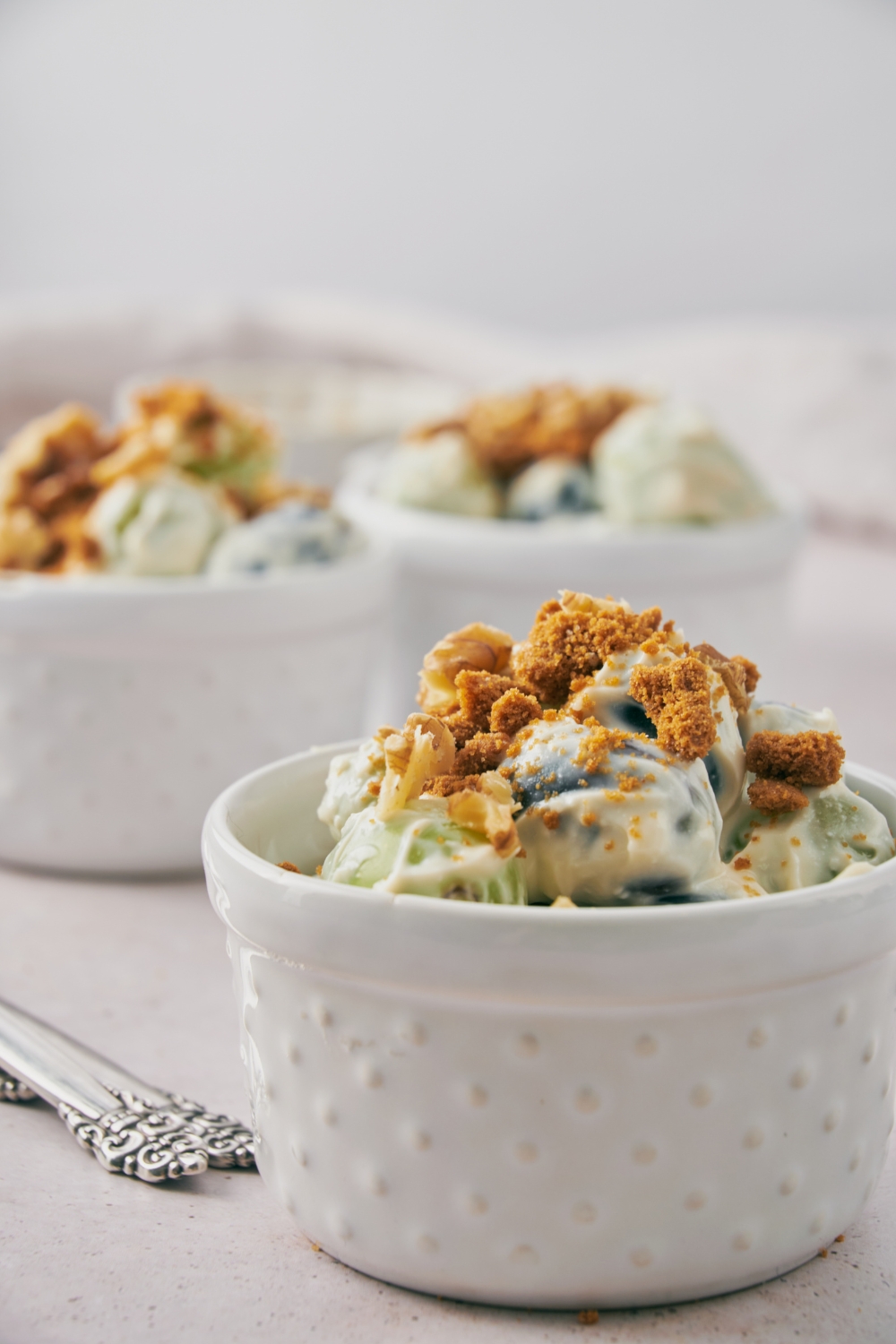 A small bowl with grape salad topped with chopped nuts and crumbled spiced cookies.