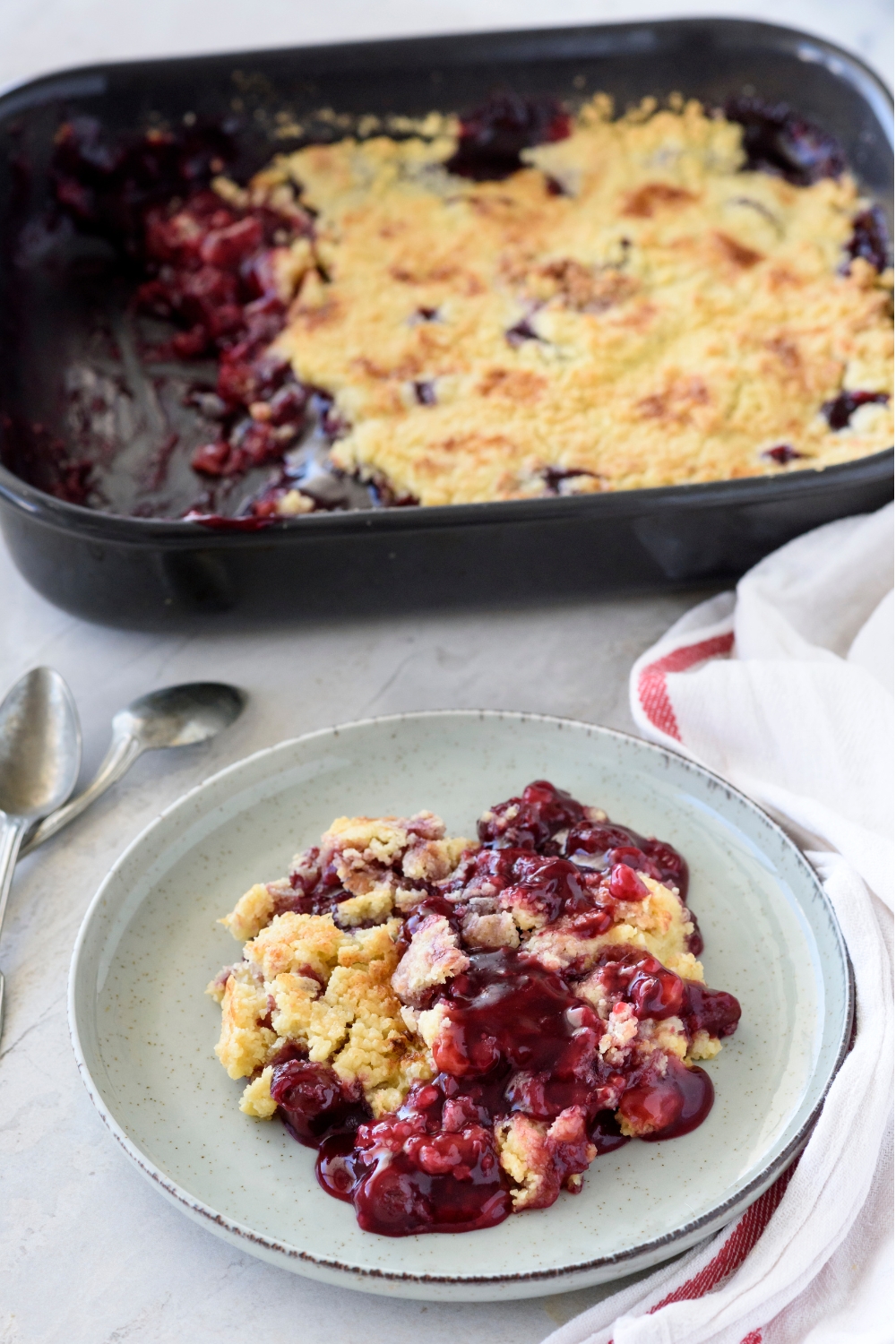 A pan with cherry dump cake. A plate with a serving of dump cake is next to the pan.