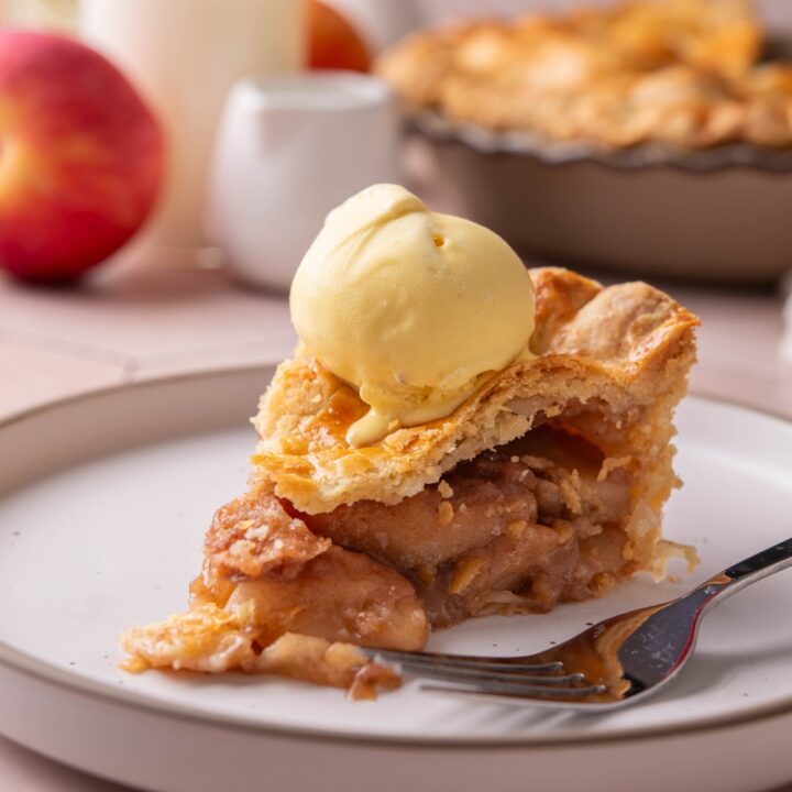 A plate with a slice of apple pie topped with a scoop of vanilla ice cream.