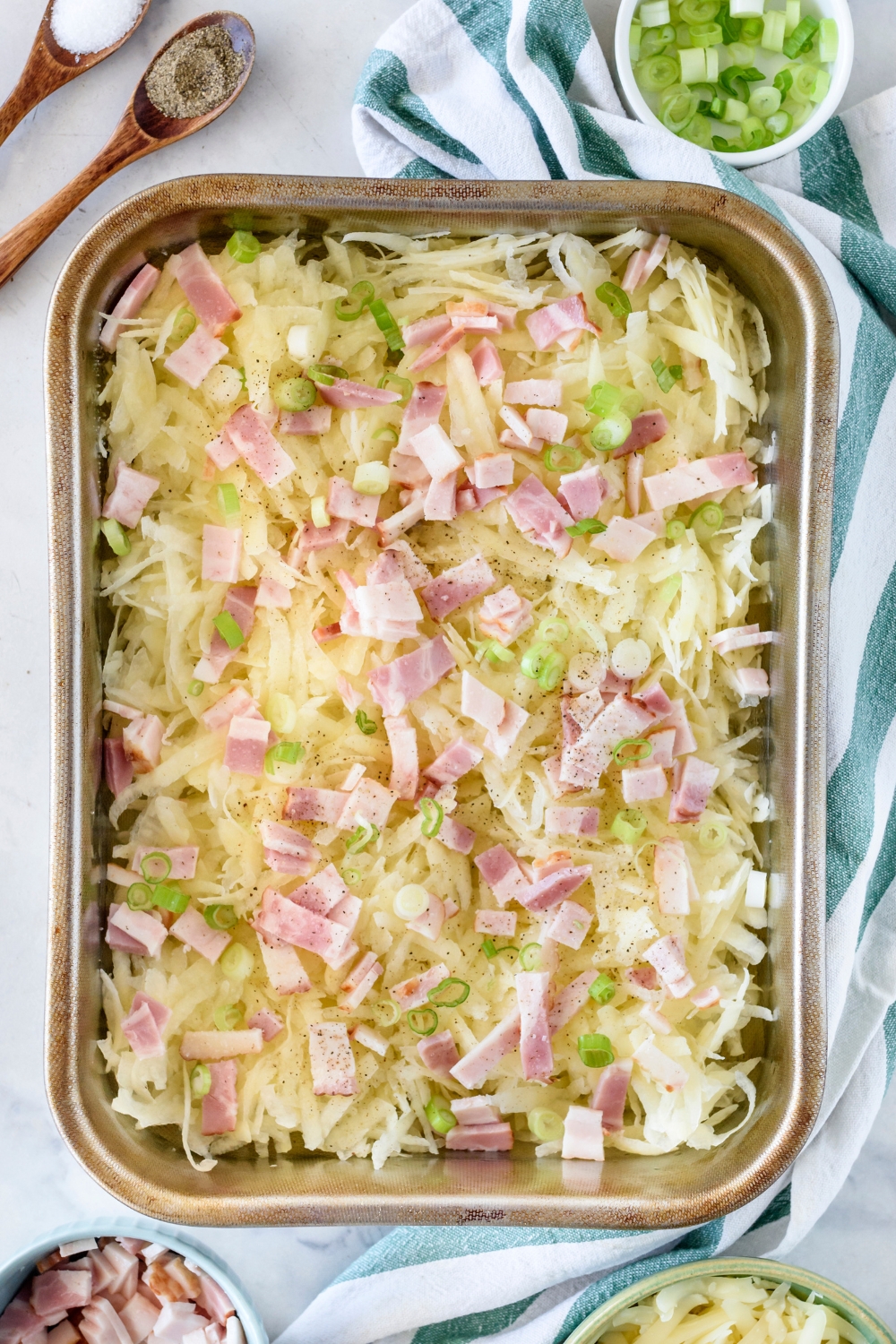 A casserole dish with chopped green onions and diced thick cut bacon added to the hash browns.