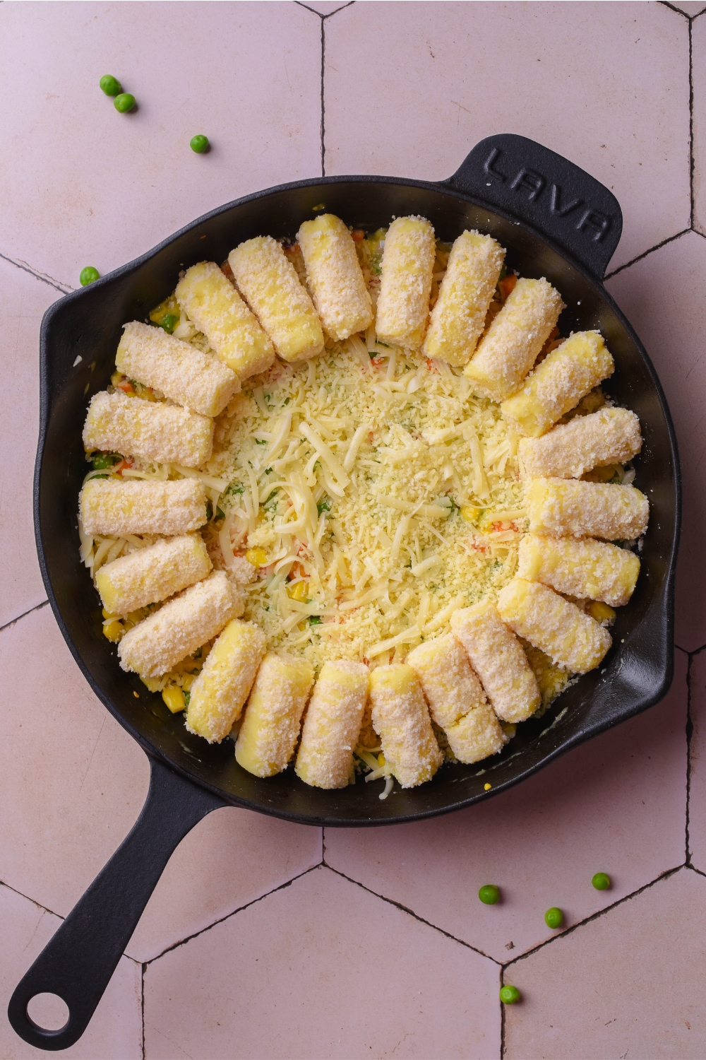 A cast iron skillet with tater tots being placed on top of the cheesy veggies.