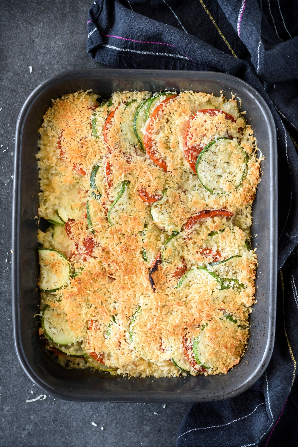 A baking dish with baked golden brown zucchini tomato casserole.