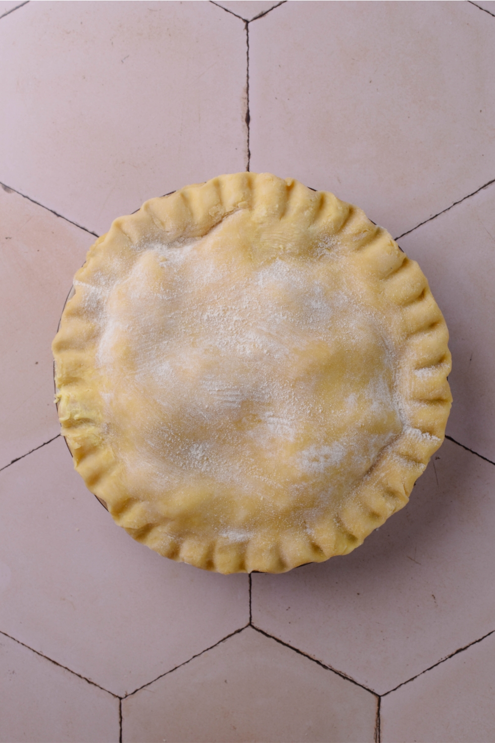 A pie dish with the top crust being added.