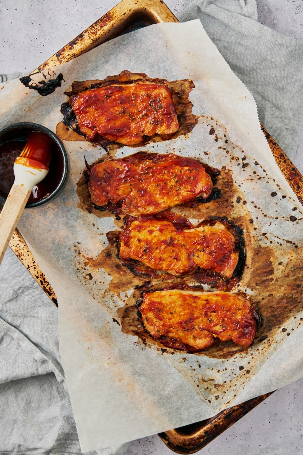 Four baked pork chops coated with BBQ sauce on a parchment paper lined baking sheet.