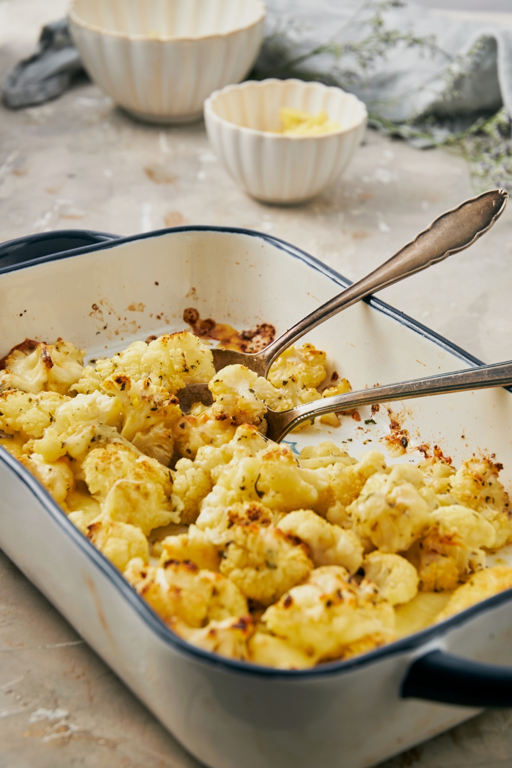 A baking dish with baked cheesy cauliflower and two spoons in it ready to serve.
