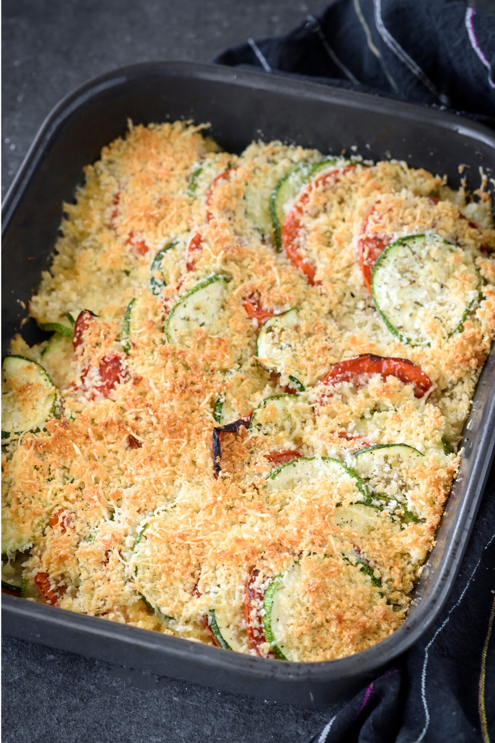 A baking dish with baked golden brown zucchini tomato casserole.