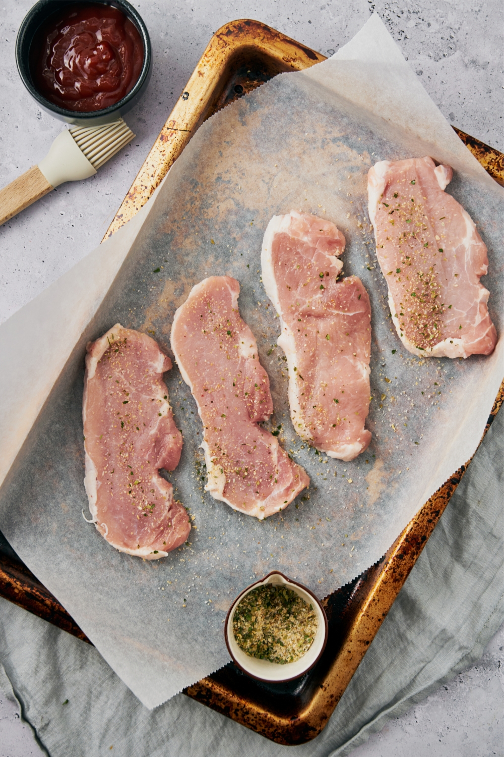 Four raw pork chops on a parchment paper lined baking sheet.