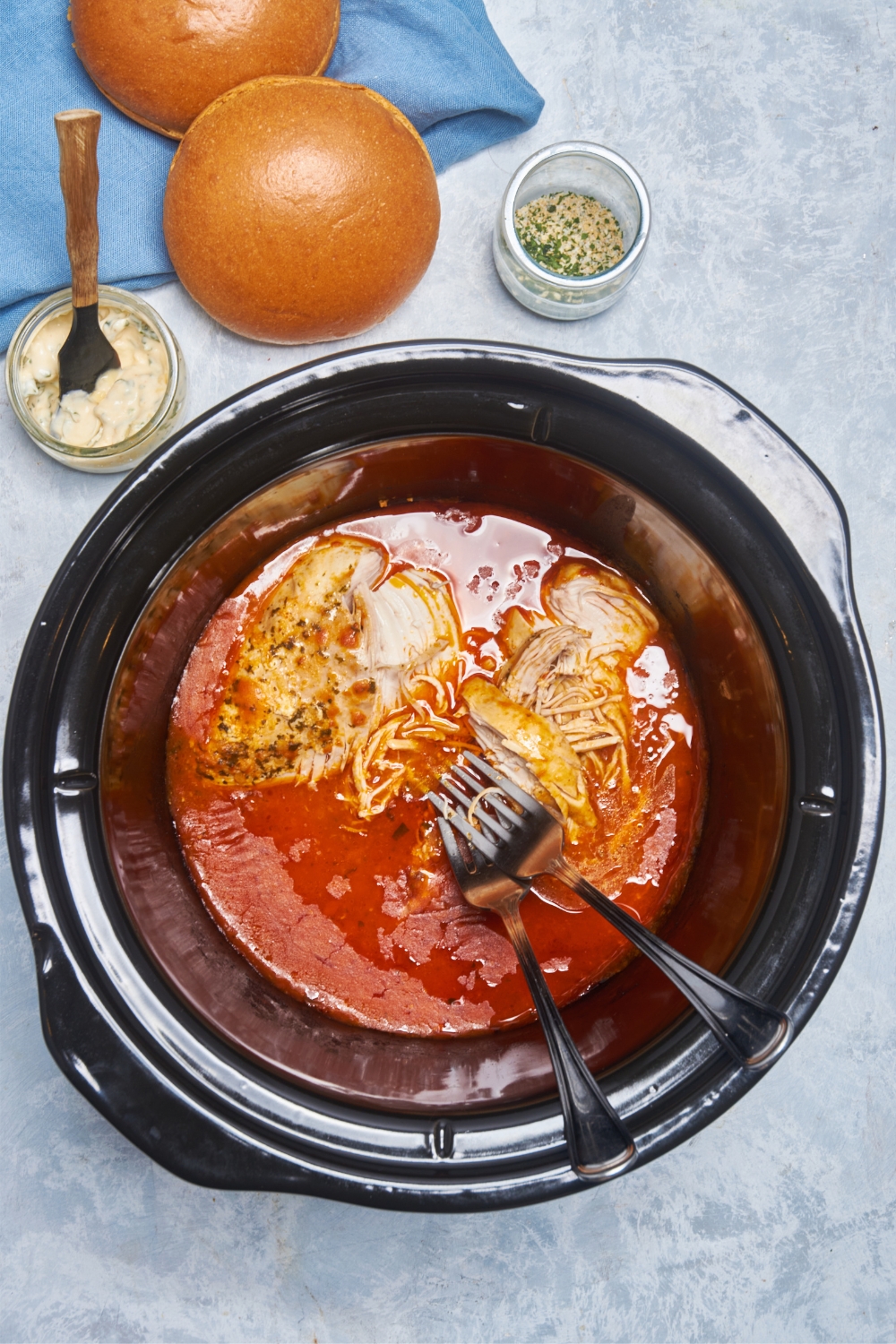 Two forks in a crock pot filled with half-shredded buffalo chicken and sauce.