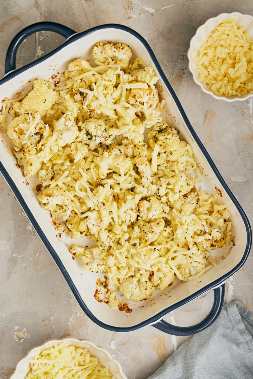 A casserole dish with a layer of cauliflower and shredded cheese on top of it.