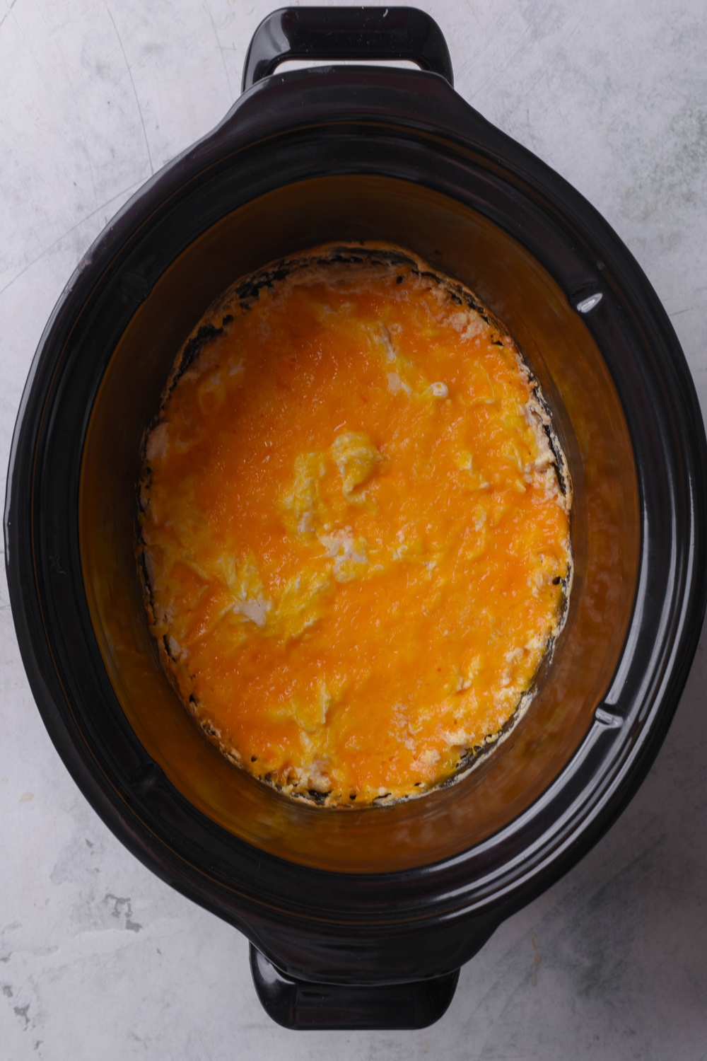 A crockpot with hash brown casserole topped with melted cheddar cheese.