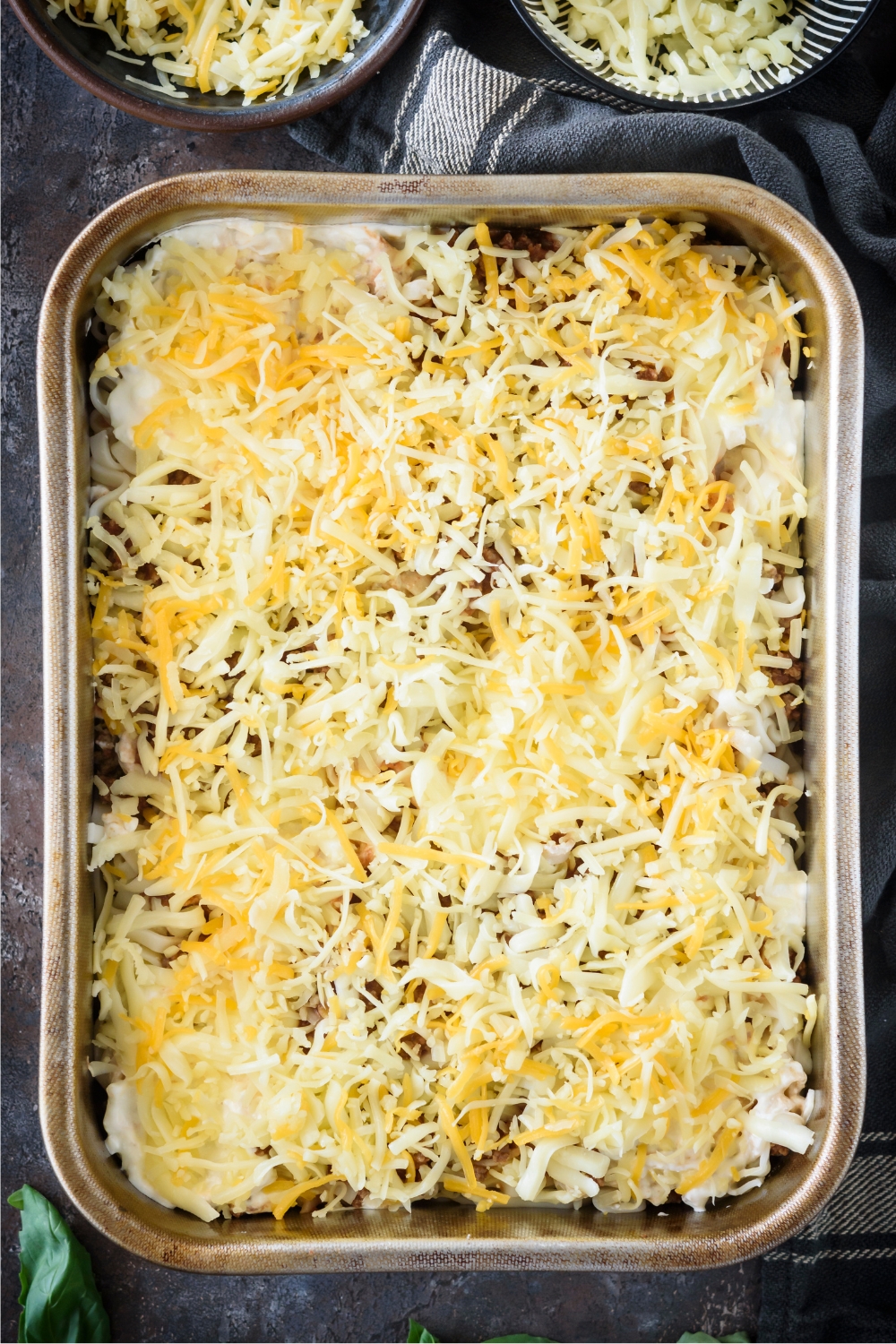 Shredded cheese on top of a ground beef amish casserole in a baking dish.