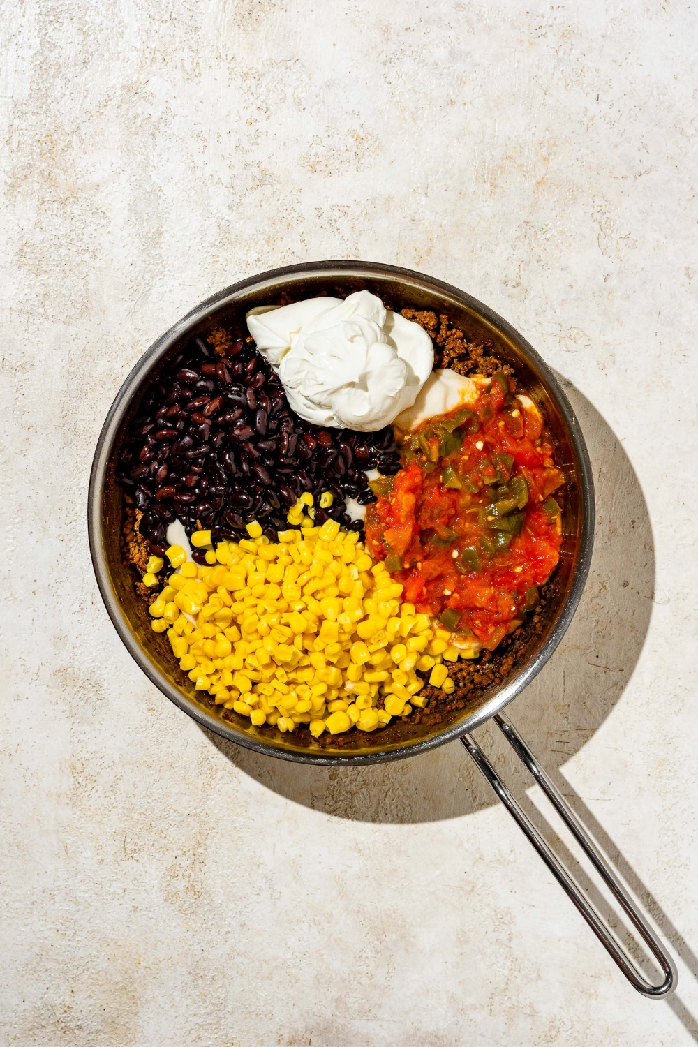 Sour cream, black beans, corn, and tomatoes in a skillet.