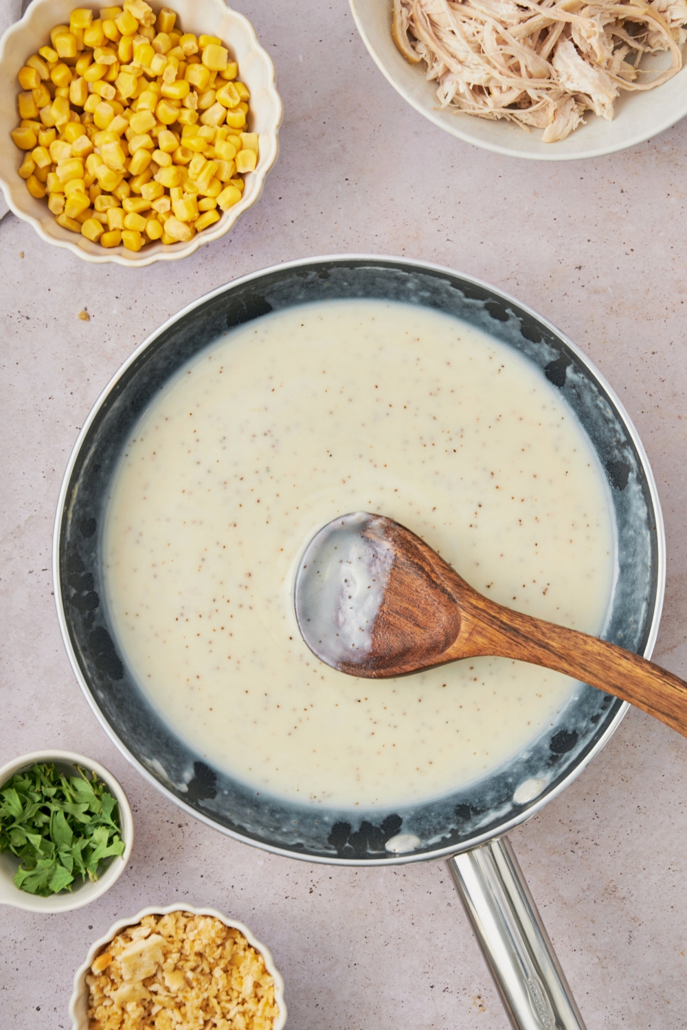 A wooden spoon in a skillet that's filled with a white cream sauce.