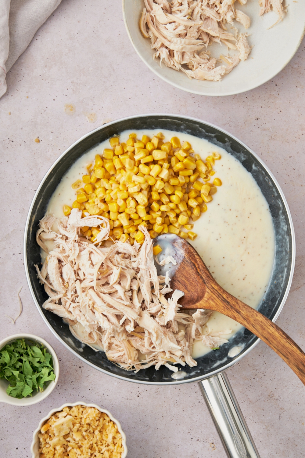 Shredded chicken and corn in a cream sauce in a skillet.