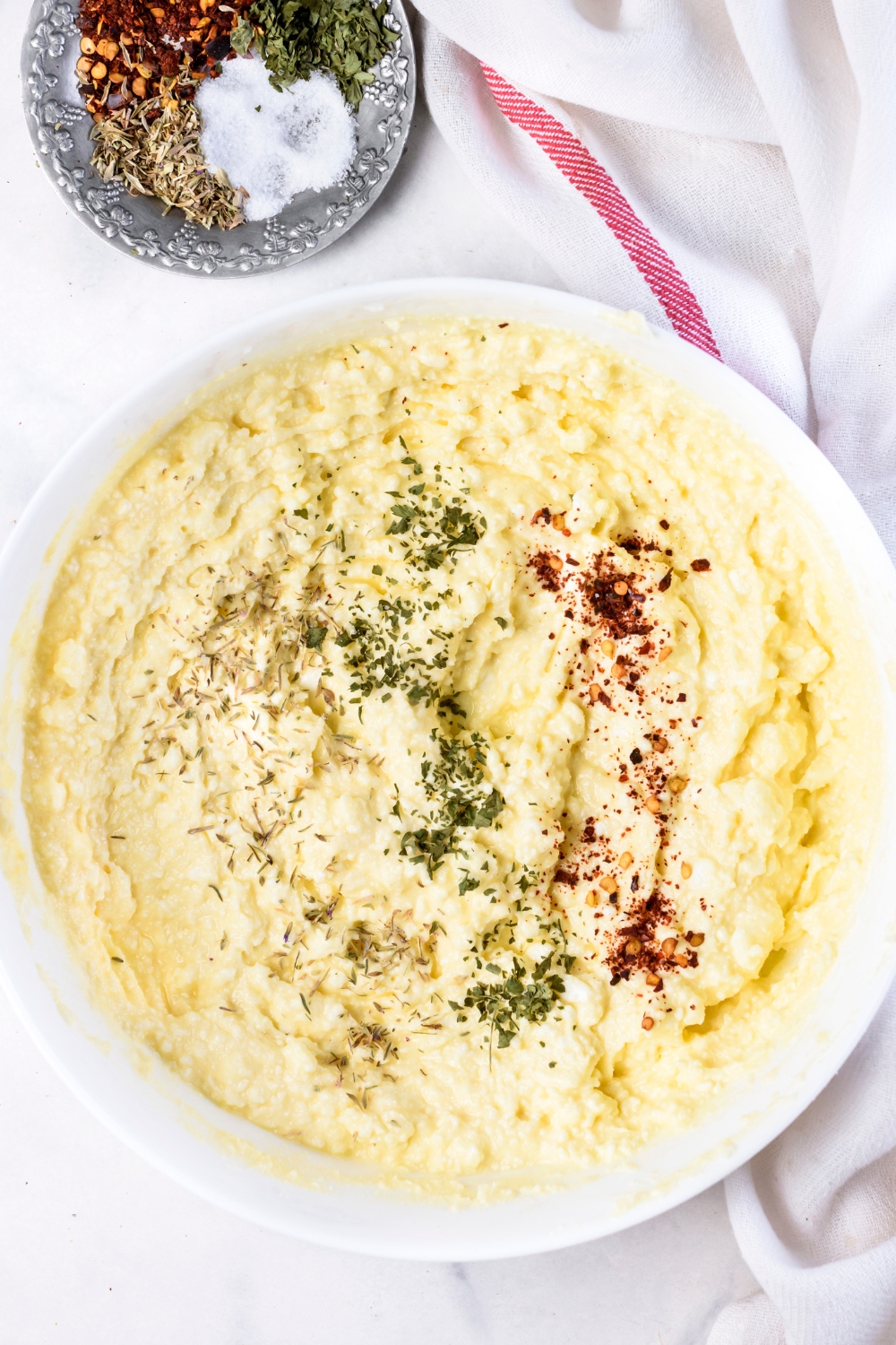 A mixing bowl with ricotta cheese and seasonings.