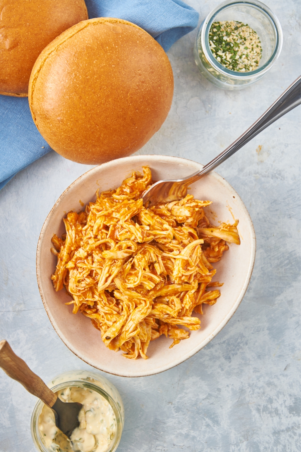 Shredded crock pot buffalo chicken in a small white bowl with a fork.