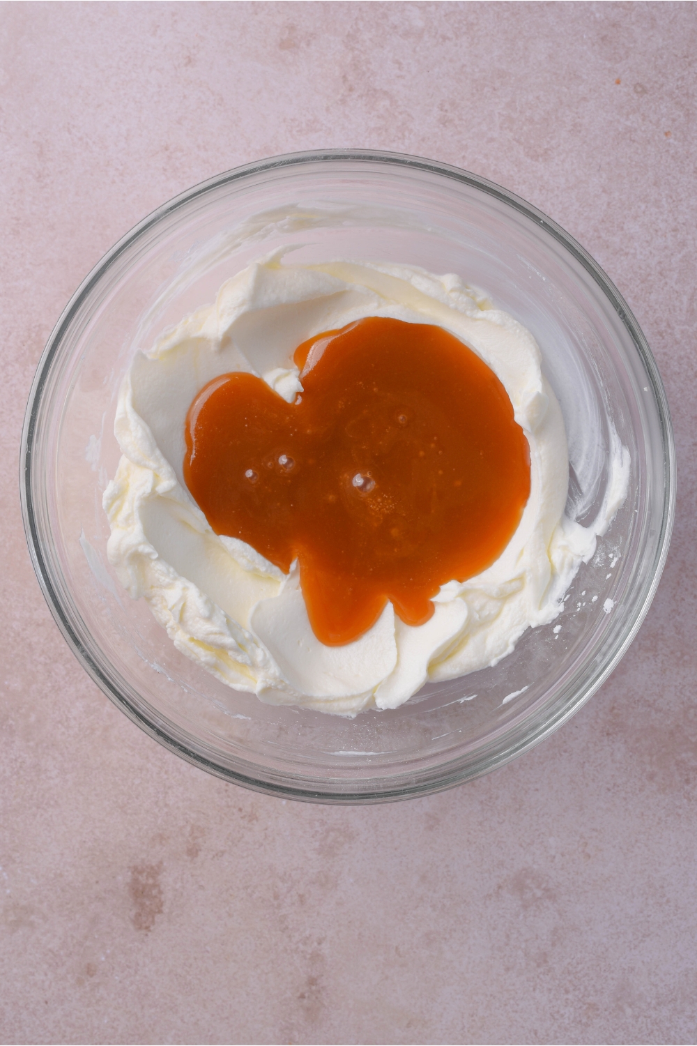Caramel sauce on top of cream cheese mixture in a glass bowl on top of a white counter.