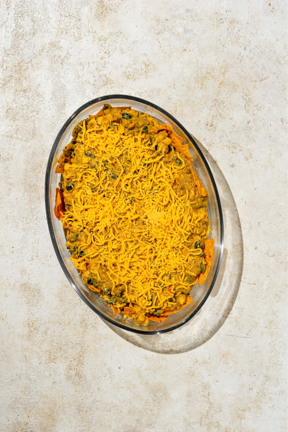 Shredded cheese on top of dorito casserole in a baking dish.