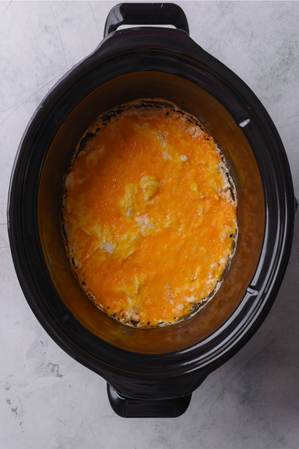 A crockpot with cooked chicken enchilada casserole.