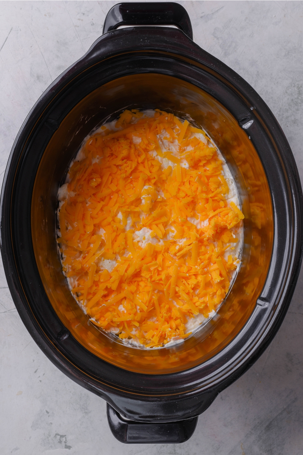 A crockpot with hash brown mixture topped with cheddar cheese.