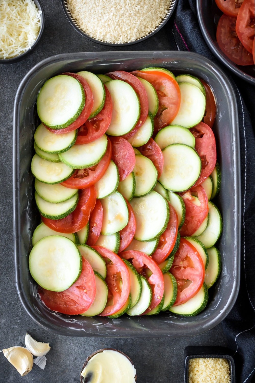A baking pan with sliced zucchini and tomatoes placed in a layer.