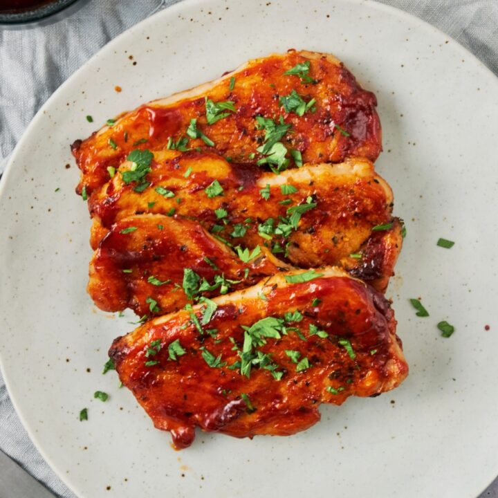 Three bbq pork chops overlapping one another on a white plate on a grey tablecloth.