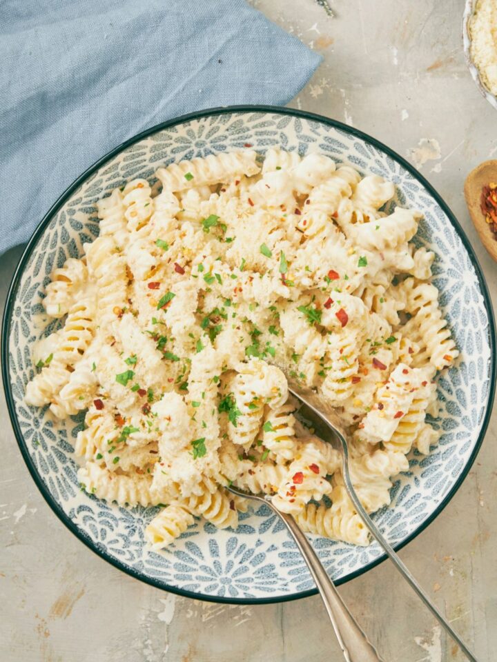 Spiral pasta noodles that are coated in a cream cheese sauce in a blue bowl on top of a grey counter.