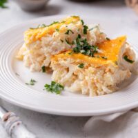 A plate with two squares of hash brown casserole garnished with chopped parsley.