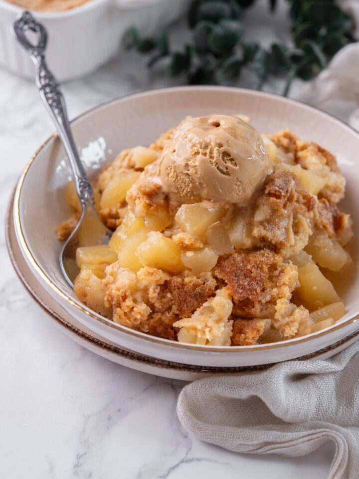 A bowl with pineapple dump cake topped with a scoop of ice cream.
